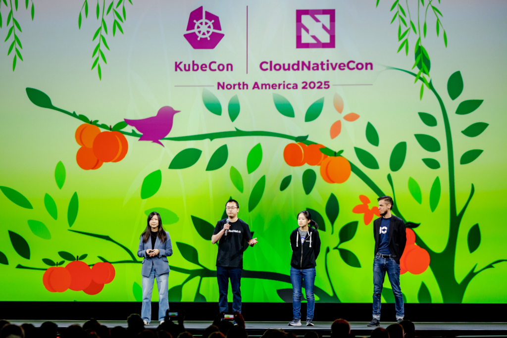 KubeCon stage with 4 persons in it, one of them talking.
